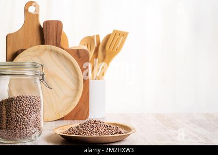 Kitchen jar with lentils next to a plate with uncooked lentils, behind cutting boards and kitchen utensils. Stock Photo