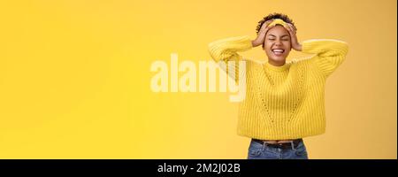 Carefree happy lucky african girl in sweater headband touching head having fun smiling relieved excited laughing out loud close eyes rejoicing spend Stock Photo