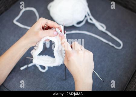 Woman hands knit white thread on circular knitting needles, dark blue blurred background. Crafting and handmade Stock Photo