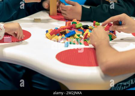 Group of crop children sitting at table and playing with colorful bricks on weekend day in playroom Stock Photo