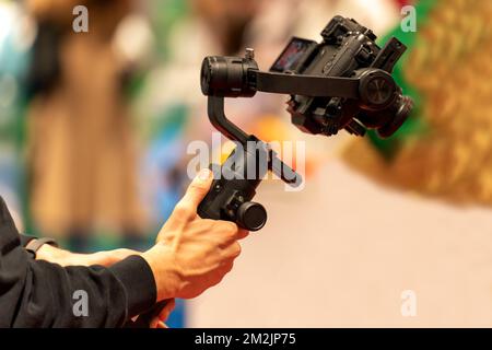 Unrecognizable man carrying stabilizer with modern camera while shooting video during public event Stock Photo