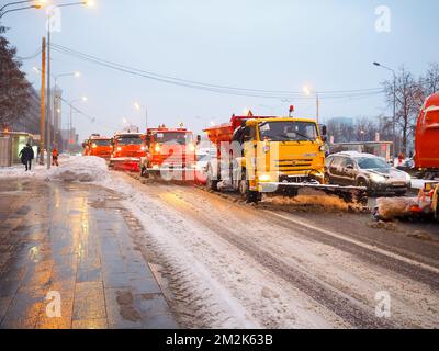 Moscow. Russia. December 14, 2022. A column of snowplows clears snow from a city street during a snowfall. Red and orange utility vehicles clean snow on a road in Moscow. Stock Photo