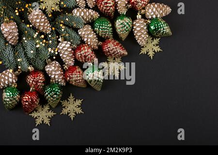 Green branches of a Christmas tree with decorations in the form of golden, red, green cones and snowflakes on a black background with twinkling festiv Stock Photo