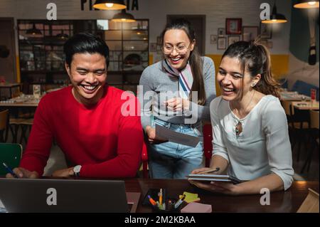 Multiracial group of three young people looking at computer laptop with smiling faces. Stock Photo