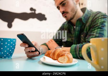cropped young bearded man using mobile phone. Guy sitting in a cafe having breakfast. Stock Photo