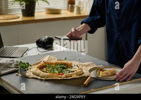 Close-up of photographer making close-up portrait of delicious pizza on her smartphone during work in studio Stock Photo