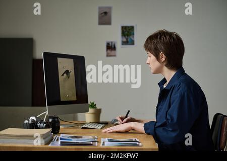 Young graphic designer retouching professional photos on computer monitor sitting at her workplace Stock Photo