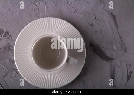 photo an empty white cup and a white embossed saucer standing on a gray irregular background Stock Photo