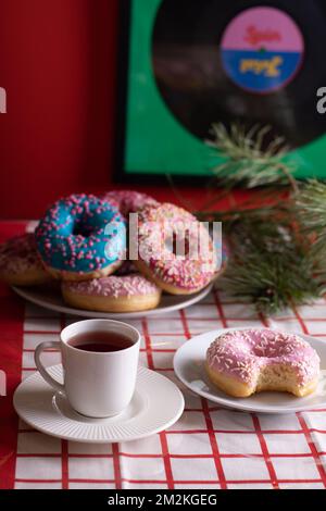 photo colorful doughnuts lying on a plate next to a light coffee cup and saucer Stock Photo