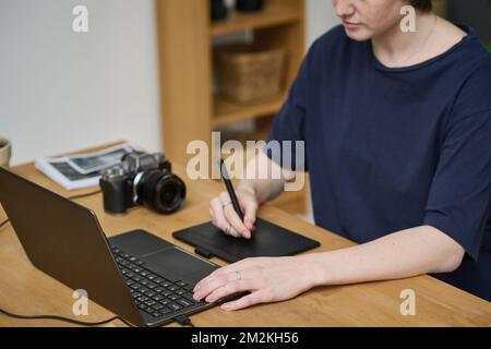 Young designer using tablet to retouch photo on laptop after shooting, she sitting at her workplace in studio Stock Photo