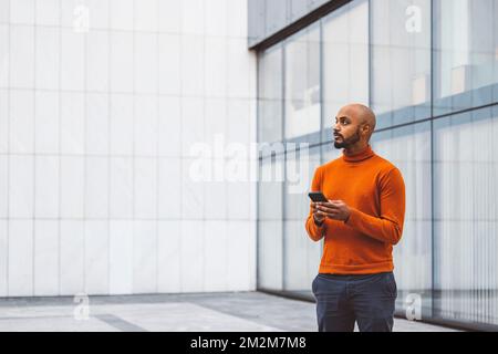 Man in orange sweater standing outside with a digital device in his hands Stock Photo