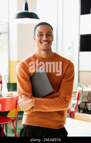 Portrait of young attractive African man holding tablet and looking at camera with smiling face. Stock Photo