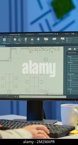 Over the shoulder shot of engineer working with architectural plans, cad software on desktop computer. Designer using arhitecture blueprints of buildings working overtime, creating and studying Stock Photo