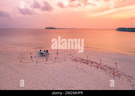 Amazing romantic dinner on the beach with candles and flowers under sunset sky. Romance and love, luxury destination dinning, exotic table setting Stock Photo