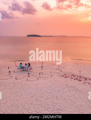 Amazing romantic dinner on the beach with candles and flowers under sunset sky. Romance and love, luxury destination dinning, exotic table setting Stock Photo