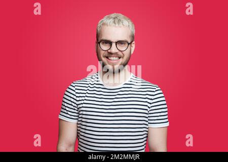 Close up portrait of happy smiling bearded hipster man with eyeglasses and looking confident at the camera isolated over red background. Happy people Stock Photo