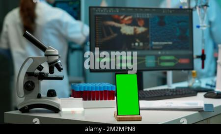 Display phone with green screen, mock up on template placed on desk in scientific lab while team of medical researcher scientists analysing virus evolution at digital monitor conducting experiment Stock Photo