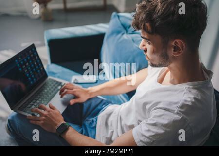 Serious caucasian man using laptop computer watching videos during free time at home interior. Shop on internet. Choose product to order online. Watch Stock Photo