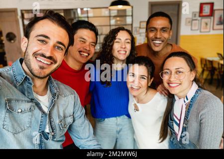 Group of six multiracial friends taking a selfie photo with smartphone in a restaurant. Stock Photo