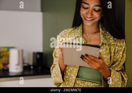 Young attractive long-haired smiling woman standing with tablet at home Stock Photo