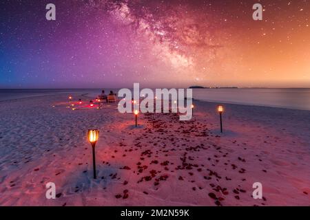 Amazing romantic dinner on the beach with candles and flowers under sunset sky. Romance and love, luxury destination dinning, exotic table setting Stock Photo