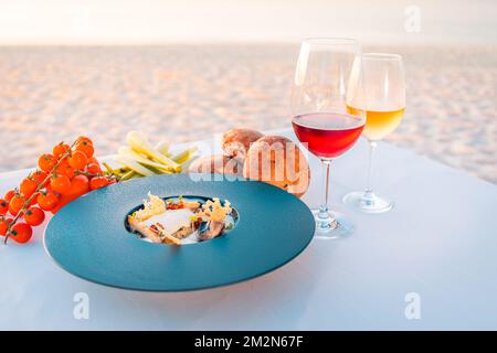 Sunset appetizer with wines and fresh vegetables on beach dinner table. Luxury food background, destination dining closeup. Stock Photo