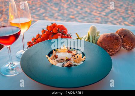 Sunset appetizer with wines and fresh vegetables on beach dinner table. Luxury food background, destination dining closeup. Stock Photo