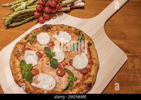 Fresh Homemade Italian Pizza Margherita with buffalo mozzarella and basil. Crusty oven-fired Italian prosciutto pizza, rustic wooden background Stock Photo
