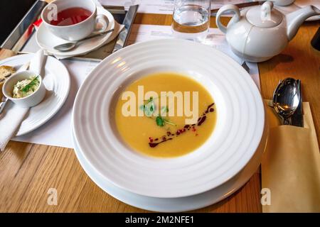 Fish soup (velouté), cup of tea, teapot, spoon, bread, butter, tray and glass of water on restaurant table. Stock Photo