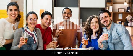 Horizontal banner or header portrait of Multiethnic group of young friends sitting at table eating pizza and drinking beer posing at camera with happy Stock Photo