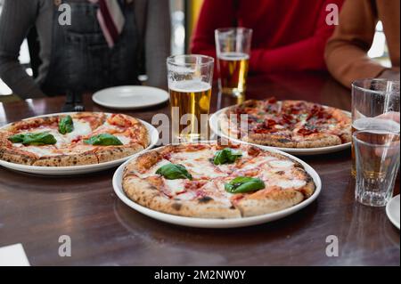 Close-up glasses of beer and pizzas on a table. Unrecognizable unfocused group of people on background. Stock Photo