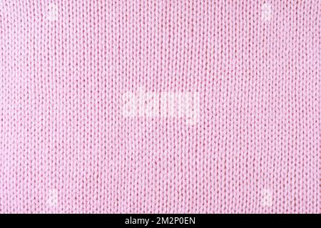 Close up background of knitted wool fabric made of viscose yarn. Pastel pink color wool knitwear texture. Abstract knitted jersey background. Fabric a Stock Photo