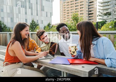 Multiracial smiling group of five teenagers students using laptop doing homework and enjoying a relaxed atmosphere outdoors at the university campus. Education concept. High quality photo Stock Photo