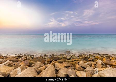 Tropical island view with beautiful sunset over the green boulders on a wave breaker. Rocks on exotic shore under colorful sky and horizon. Exotic sea Stock Photo