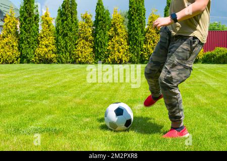 Soccer ball and boys legs close up. The teenager plays soccer on the backyard Stock Photo