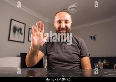 Bearded business man wave hand to camera. Web cam view of smiling young male, video call concept. Smiling, happy and working from home meeting online. Stock Photo