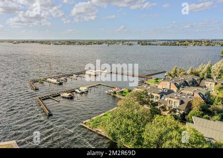 some boats in the water and houses on the other side of the lake, with clouds overhead over them to make it look like Stock Photo