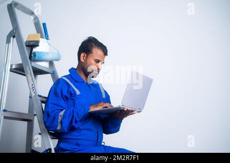 Paint worker busy using laptop at construction site - concept of renovation, technology and taking break. Stock Photo