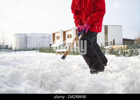 Girl shoveling snow on home drive way. Beautiful snowy garden or front yard. Teenager removing snow with a shovel in the winter Stock Photo