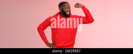 Charming cheeky friendly african-american strong guy smiling broadly proudly showing biceps raise one hand bragging muscles attend gym recommend you Stock Photo