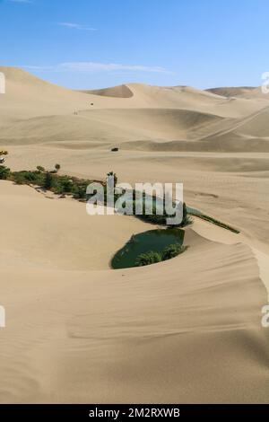 A vertical shot of the Huacachina oasis surrounded by sand dunes on a sunny day in southwestern Peru Stock Photo