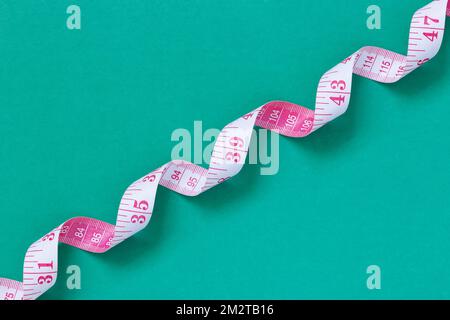 White and pink measuring tape with metric and inch markings, twisted into a spiral on a green background Stock Photo