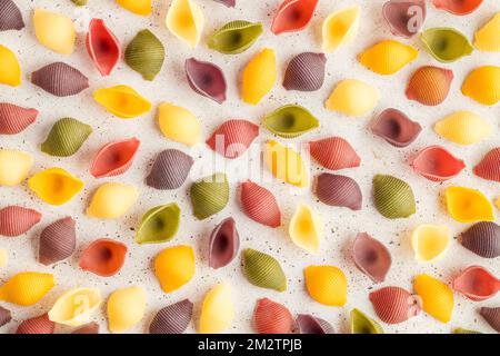 Top view of five colors pasta shells on white stone background. Colorful pasta background. Pasta with turmeric, spinach, beetroot and black carrot. Stock Photo