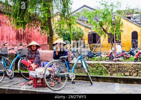 With a canal and the Japanese Covered Bridge, two Vietnamese woman enjoy a friendly chat. Stock Photo