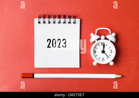 2023 desk calendar and alarm clock with wooden pencil on red cardboard. Stock Photo