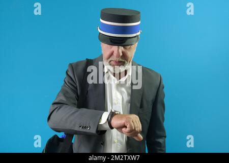 The train conductor carefully looks at his wristwatch before the train leaves. On a blue background Stock Photo