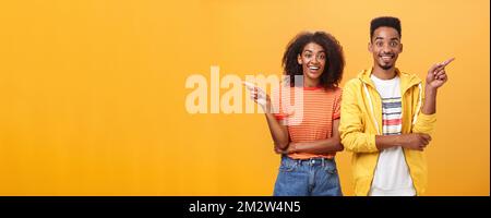 Which one telling true. Joyful and friendly good-looking couple, african american woman pointing left and dark-skinned guy right smiling broadly at Stock Photo