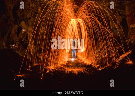 A long exposure shot of a person rotating a burning steel wool in a cave Stock Photo