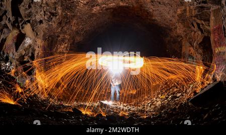 A long exposure shot of a person rotating a burning steel wool in a cave Stock Photo