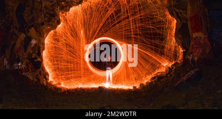 A long exposure shot of a person rotating a burning steel wool in a cave Stock Photo